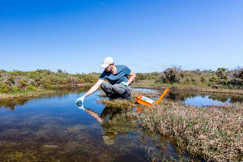 A man takes a water sample from a river on a clear, sunny day.