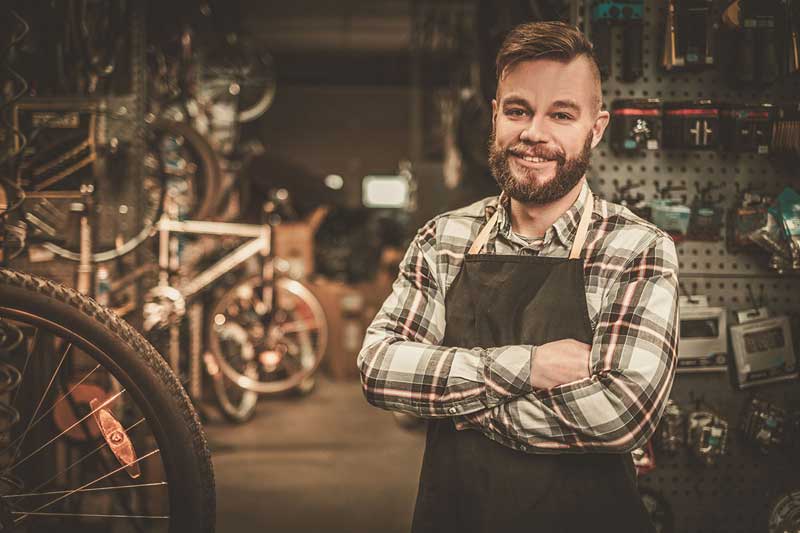 A young man smiles as he stands in his bicycle repair shop.