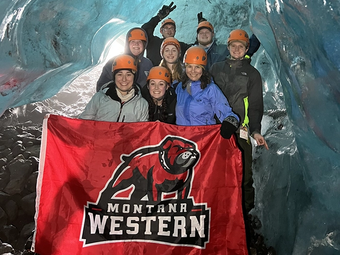 Students in an ice cave hold a Montana Western flag during a field study.