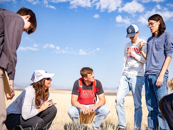 Students discuss a lesson outdoors in an open field.