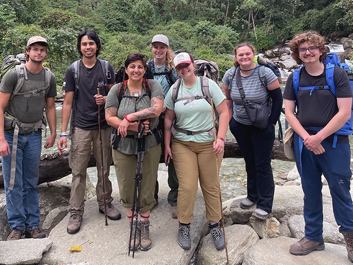 Group of student hikers with backpacks beside a rocky stream.